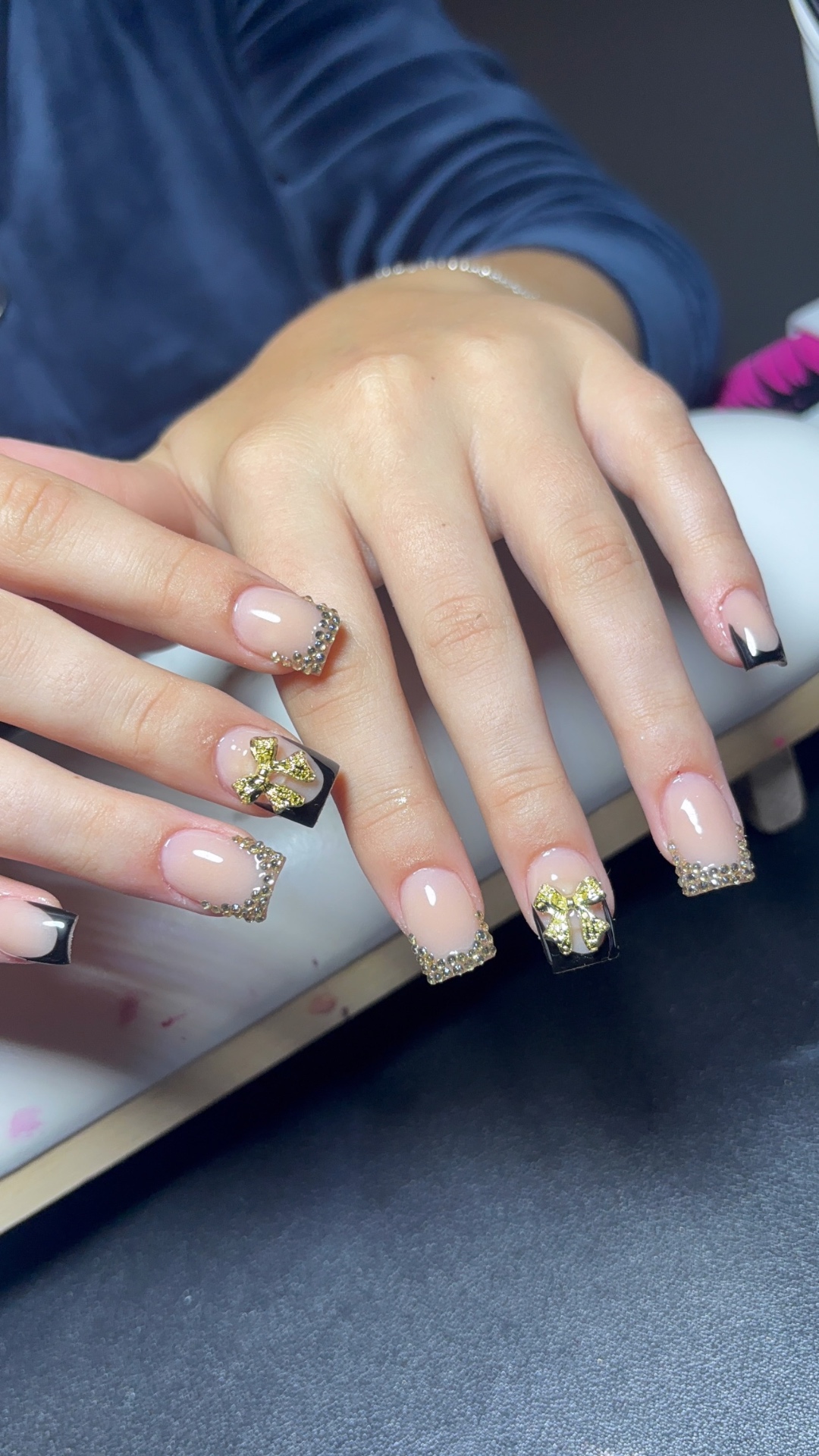 Mains aux ongles noir et or avec strass et nœuds 3D réalisée au studio